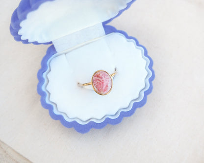Ring with a pink and gold design on a white fabric background. Tiny Scallop Shell Gold Ring on stone displayed. Tiny Pink Scallop Shell Bezel Ring, 18k gold stainless steel, handpicked scallop shell from the beach of Portugal.
