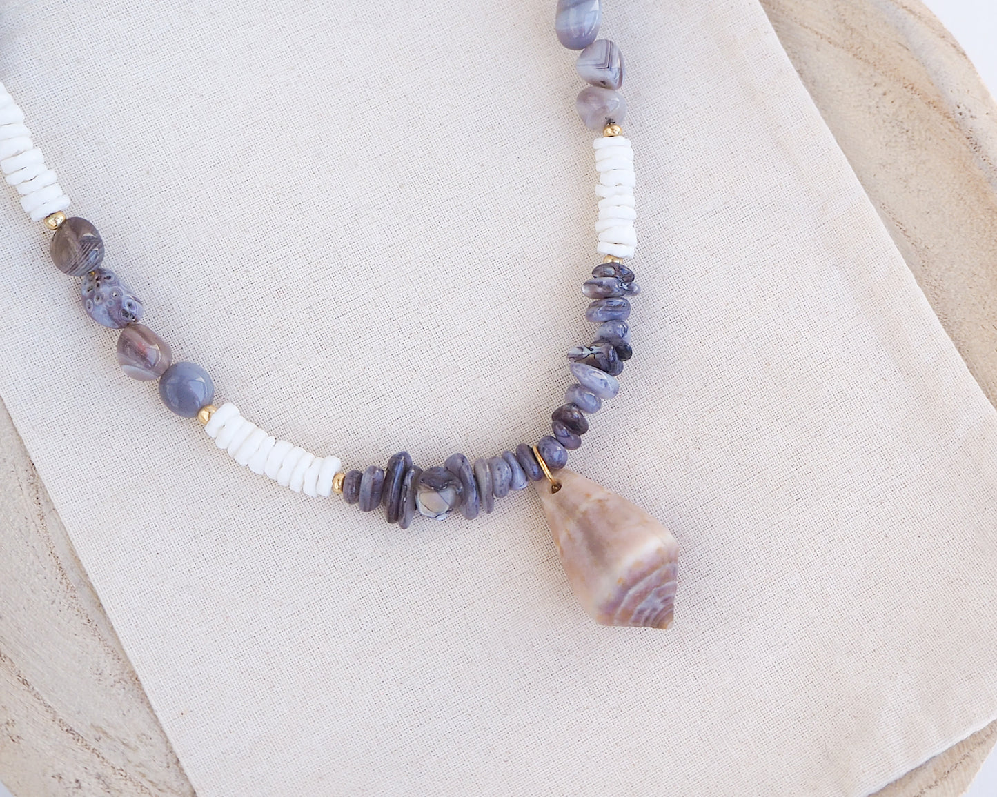 Necklace with grey and white beads and a large cone shell pendant on a light background. A necklace with a mediterranean cone shell paired with Botswana agate gemstone beads and white shell beads. The shell is a mediterranean cone shell from Portugal and is about 3,5 cm. The color of the shell is brown.