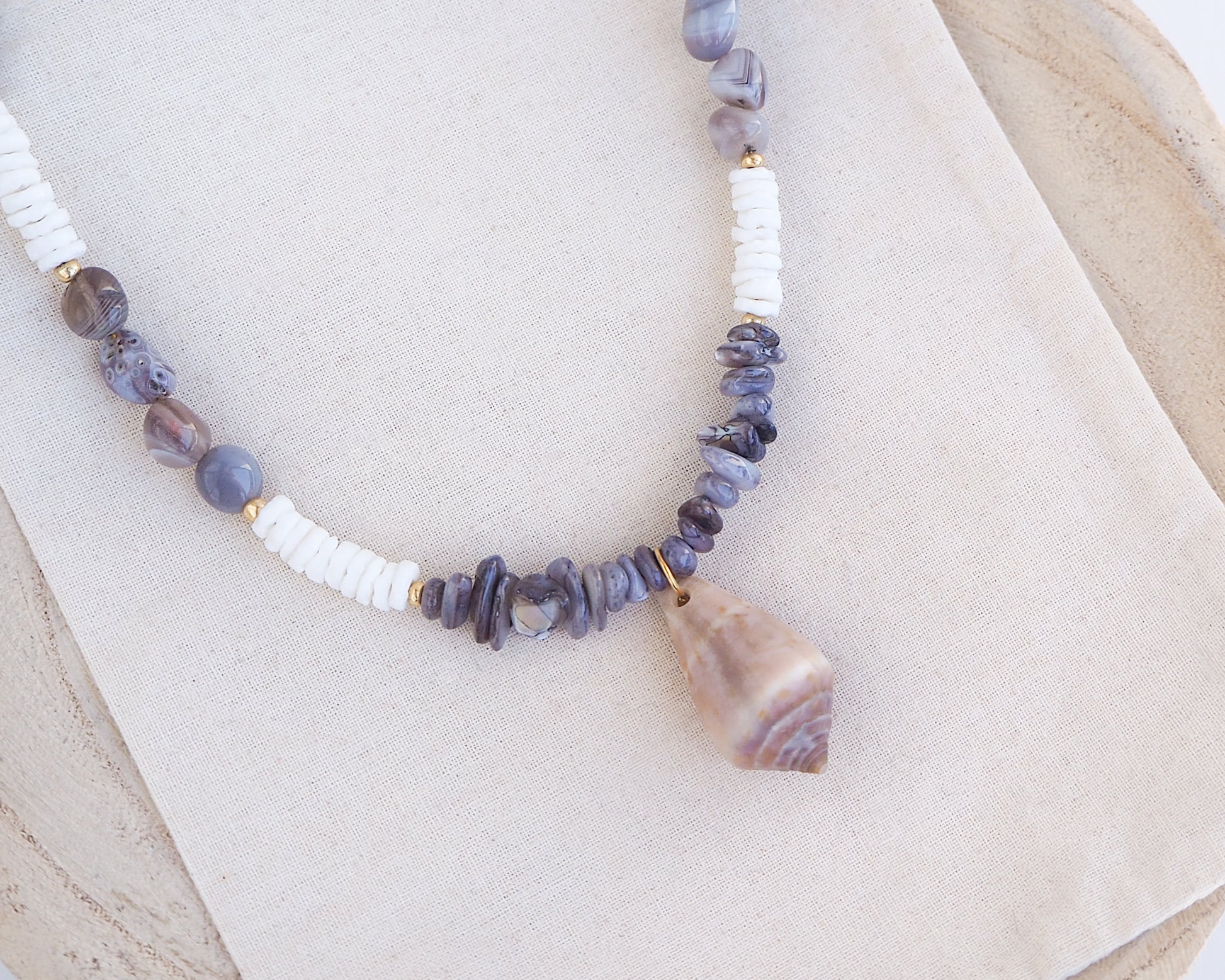 Necklace with grey and white beads and a large cone shell pendant on a light background. A necklace with a mediterranean cone shell paired with Botswana agate gemstone beads and white shell beads. The shell is a mediterranean cone shell from Portugal and is about 3,5 cm. The color of the shell is brown.