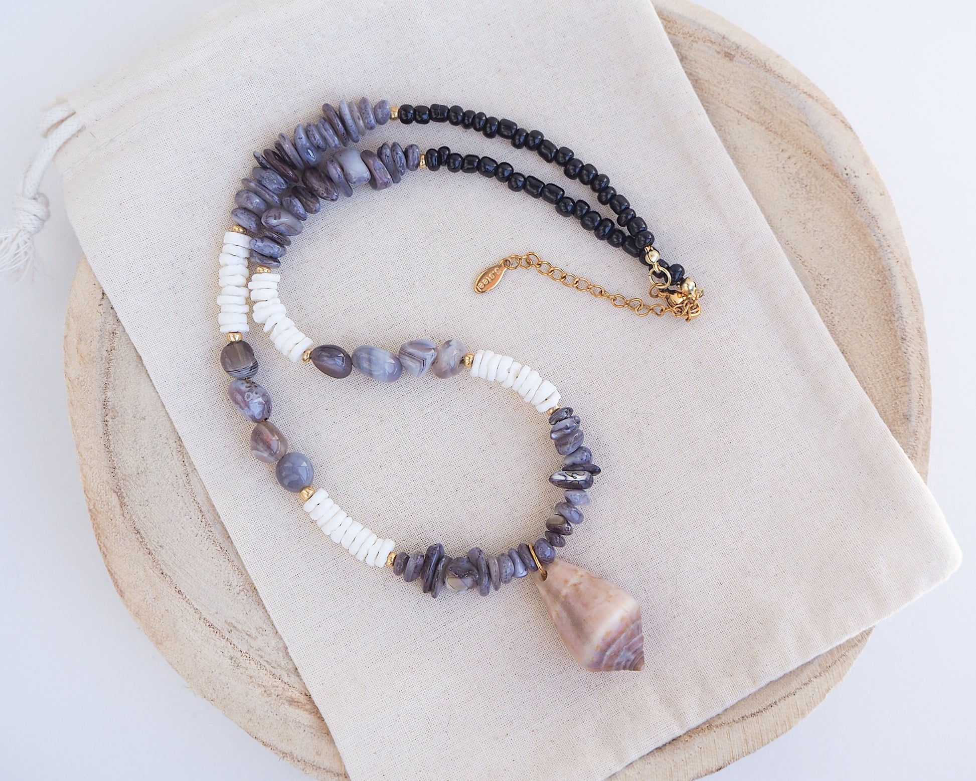 Front view of a necklace with grey and white beads and a large cone shell pendant on a light background. A necklace with a mediterranean cone shell paired with Botswana agate gemstone beads and white shell beads. The shell is a mediterranean cone shell from Portugal and is about 3,5 cm. The color of the shell is brown.