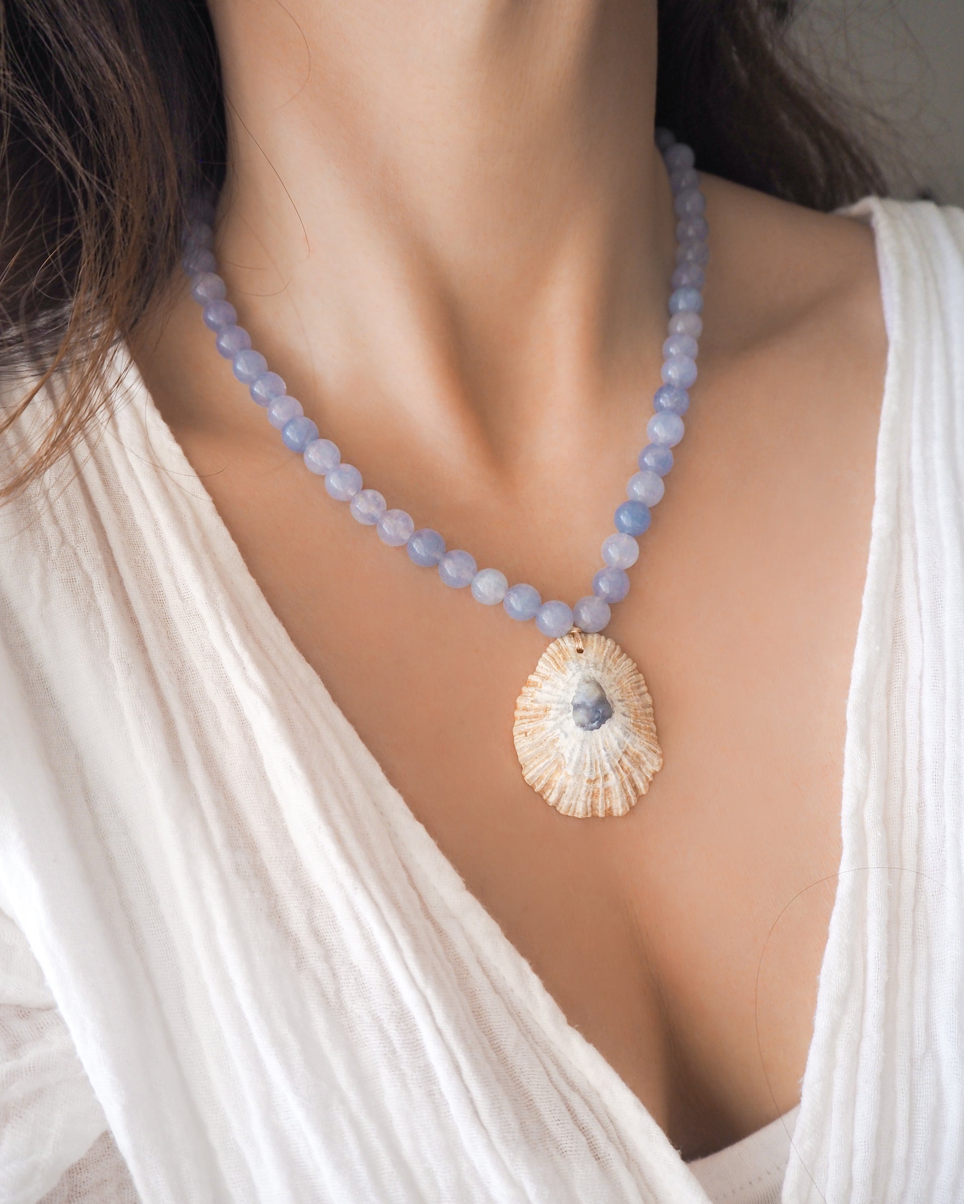 Model wearing a Big Limpet shell necklace paired with aquamarine gemstone beads. The shell is a Mediterranean Limpet shell from Portugal and is about 5 cm. The color of the shell is ivory beige with a grey blue center