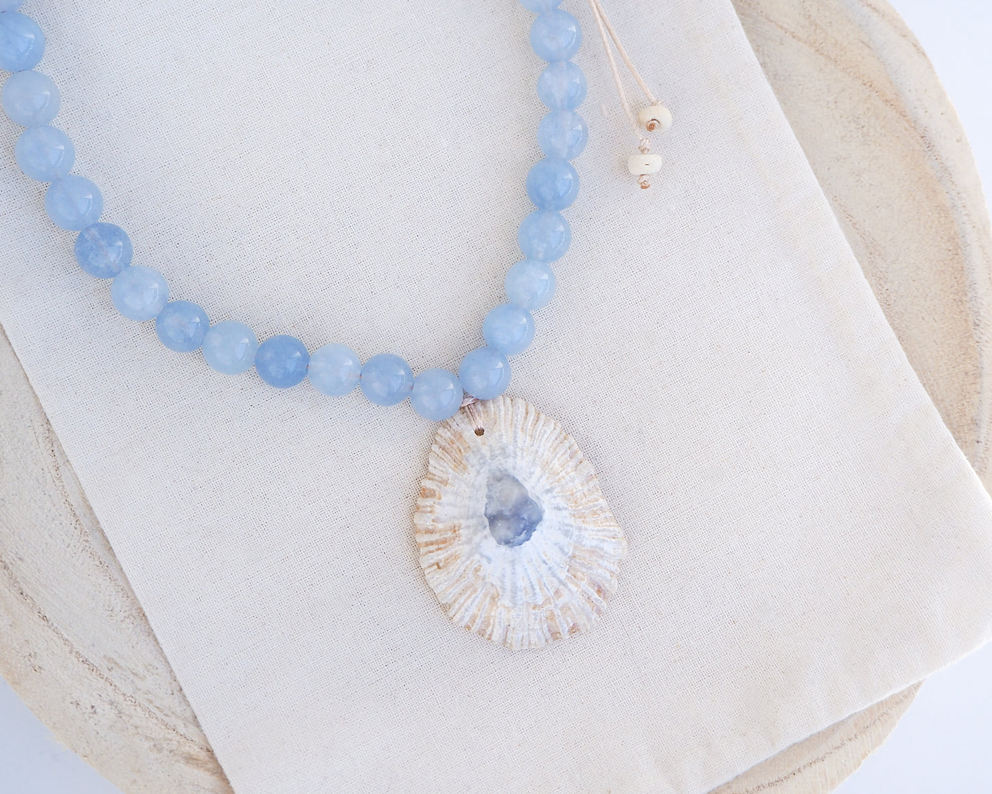 Close up of a Big Limpet shell necklace paired with aquamarine gemstone beads. The shell is a Mediterranean Limpet shell from Portugal and is about 5 cm. The color of the shell is ivory beige with a grey blue center