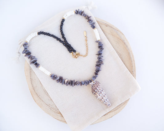 Necklace with grey stone and white shell beads and a large horn shell pendant on a light background. A necklace with a mediterranean horn shell shell paired with grey stone beads and white shell beads. The shell is a mediterranean horn shell from Portugal and is about 5 cm. The color of the shell is white with dark pattern.