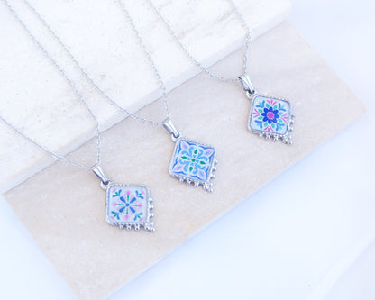 Close up of 3 silver Portuguese Tile Necklace Floral Garden on stone displayed. Made with stainless steel or silver stainless steel and the colorful floral pendant are inspired by the Portuguese Azulejo design pattern. 