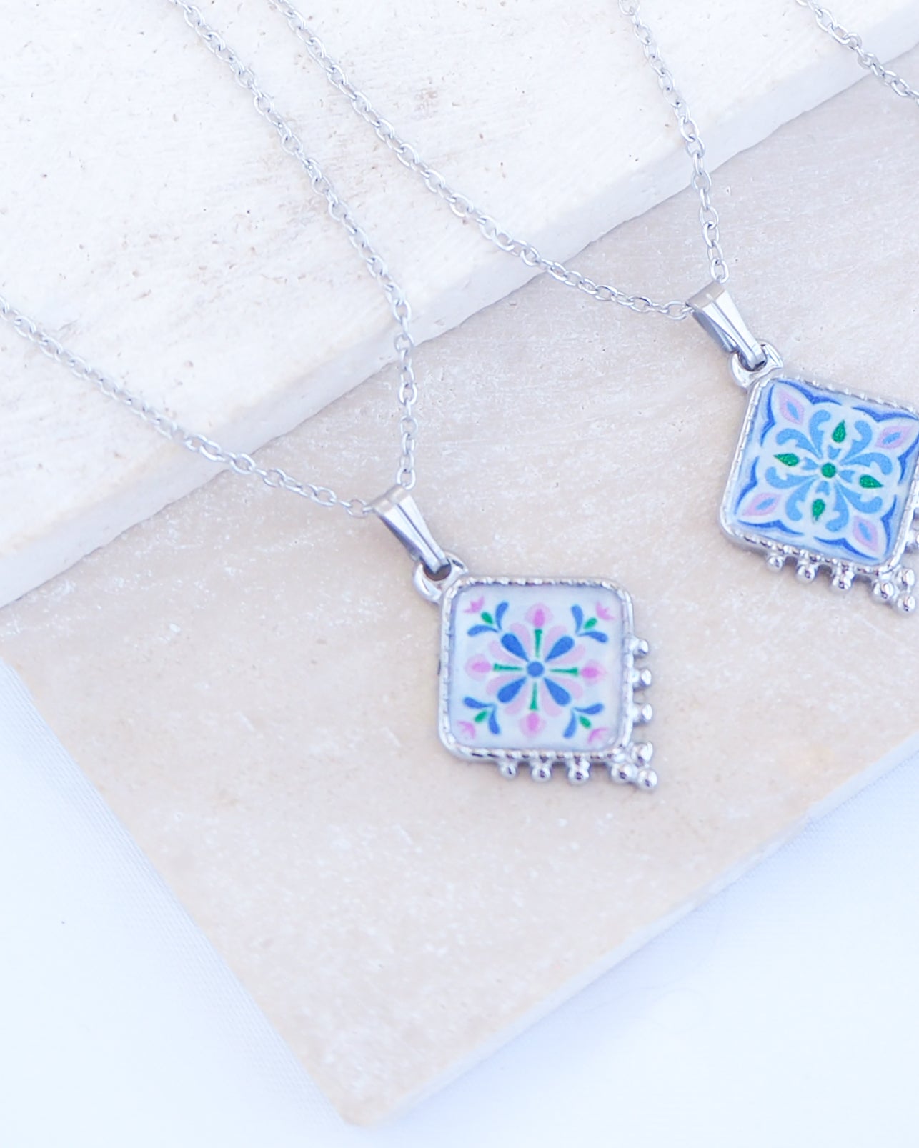 Close up of silver portuguese Tile Necklace Floral Garden on stone displayed. Made with stainless steel or silver stainless steel and the colorful floral pendant are inspired by the Portuguese Azulejo design pattern. 