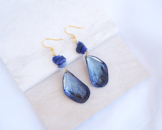 Stone displayed with handmade blue mussel shell earring with a gold fishhook, a small dark blue lapis lazuli gemstones. The mussel shells were handpicked from the beaches of Portugal and they have a dark blue and white coloring.