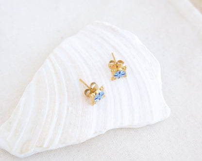 Front view of A pair of small gold stud earrings with blue and white Portuguese tile pattern, displayed on a white seashell against a soft off-white background. Made with gold stainless steel and blue white center pattern that are inspired by the Portuguese Azulejo design pattern. 
