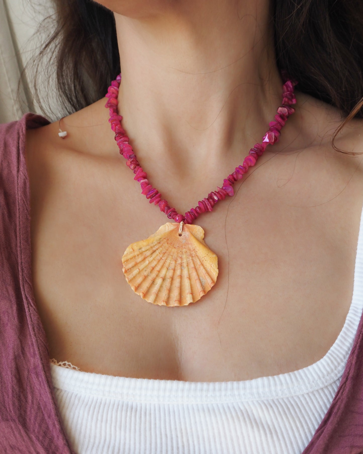 Model wearing a big scallop shell necklace with fuchsia pink stone beads. The shell is a great scallop shell from Portugal and has orange coral color. 