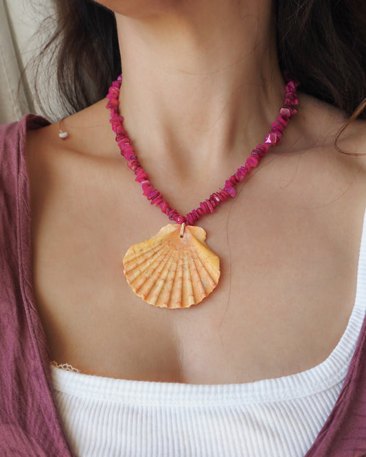 Model wearing a big scallop shell necklace with fuchsia pink stone beads. The shell is a great scallop shell from Portugal and has orange coral color. 