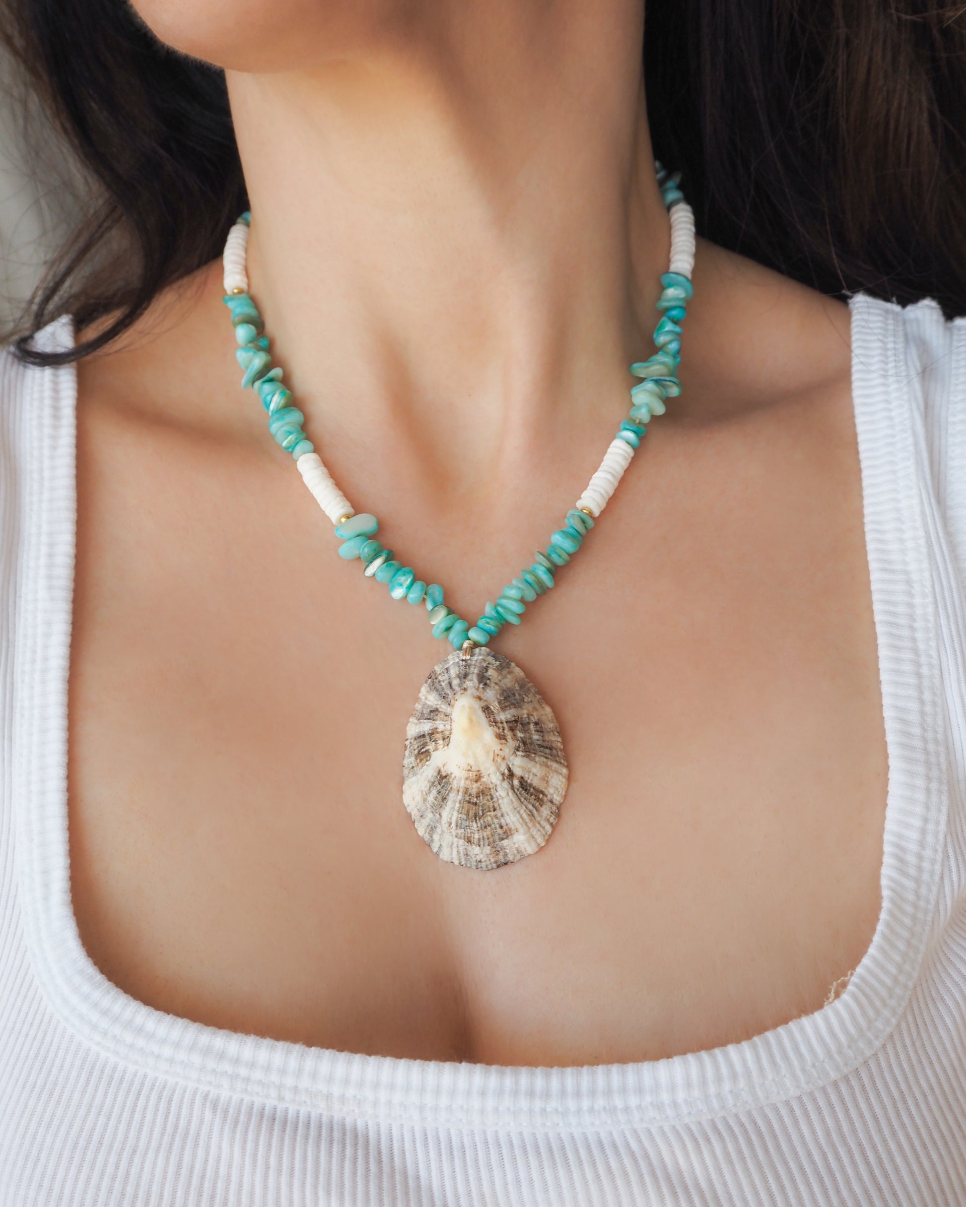 Model wearing a big limpet shell necklace with turquoise stone beads and white shell beads. The limpet shell is handpicked from Portugal and has white contrast dark brown stripes