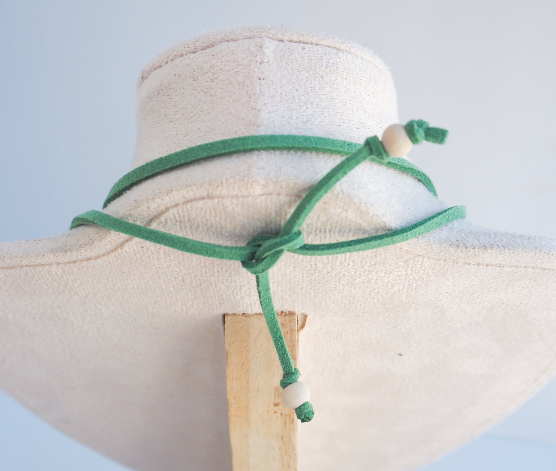 A green adjustable cord necklace with wooden beads, displayed on a cream fabric jewelry bust against a light blue background.