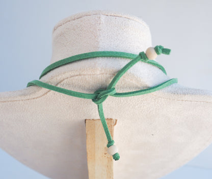 A green adjustable cord necklace with wooden beads, displayed on a cream fabric jewelry bust against a light blue background.