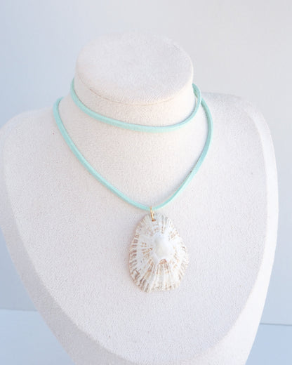 A necklace displayed on a white jewelry bust, featuring a turquoise cord with a large white seashell pendant and a thin mint turquoise wrap around the neck area.