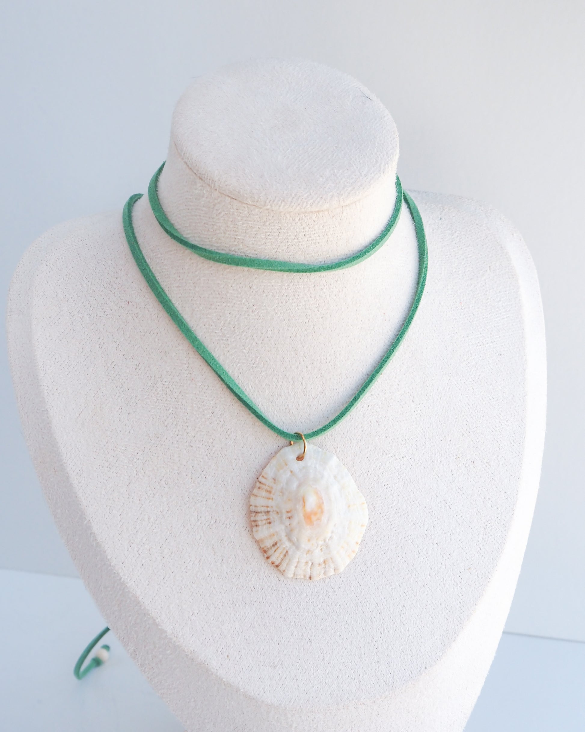 A mannequin with a shell pendant necklace with a green cord and white beads, with a white background. The shell is a limpet shell from Portugal and is about 5 cm. The color of the shell is off white and it has an orange center.