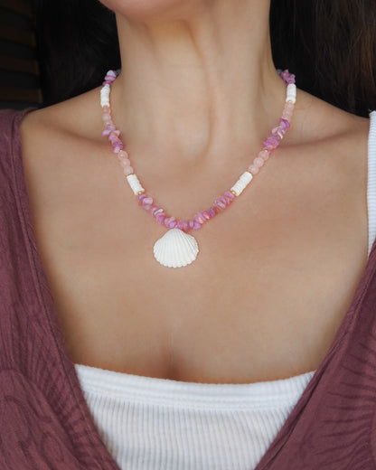 Model wearing a pink and white beaded necklace with a large seashell pendant. A necklace with pink and white beads and a large cone shell pendant on a light background. A necklace with a mediterranean cockle shell paired with rose quartz gemstone beads, soft pink stones and white shell beads. The shell is a mediterranean cockle shell from Portugal and is about 3 cm. The color of the shell is white.