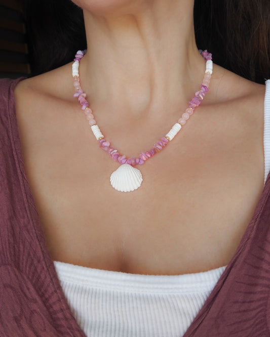 Model wearing a pink and white beaded necklace with a large seashell pendant. A necklace with pink and white beads and a large cone shell pendant on a light background. A necklace with a mediterranean cockle shell paired with rose quartz gemstone beads, soft pink stones and white shell beads. The shell is a mediterranean cockle shell from Portugal and is about 3 cm. The color of the shell is white.