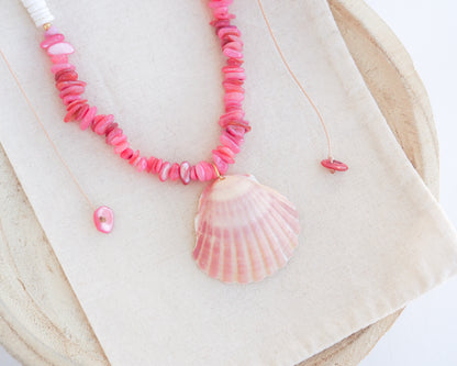 Close up of a necklace with pink and white beads and a shell pendant on light cotton displayed. A necklace with a big pink scallop shell paired with rose quartz gemstone beads, coral pink stones and white shell beads. The shell is a pilgrim's scallop shell handpicked from Portugal and is about 5 cm. The color of the shell is soft pink.