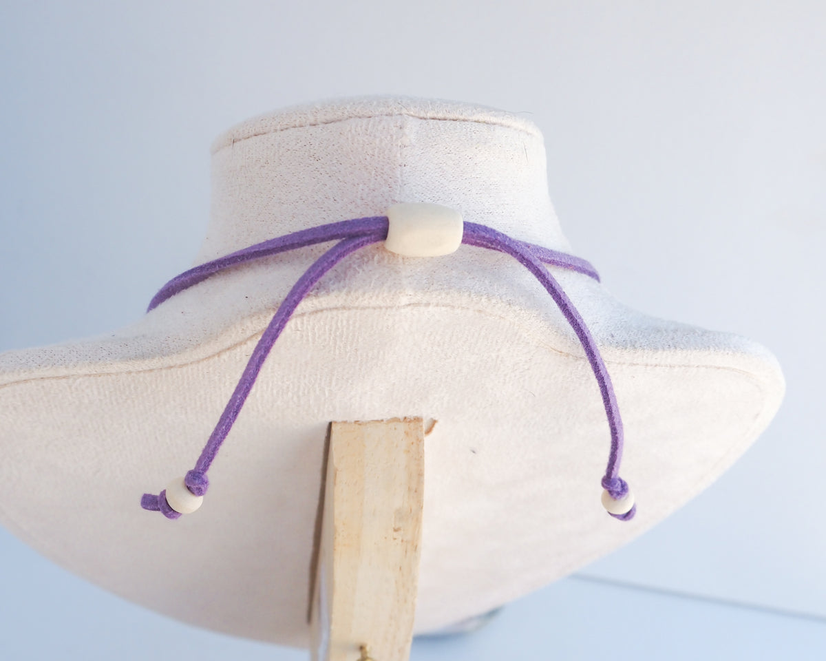 A purple adjustable cord necklace with wooden beads displayed on a cream-colored fabric jewelry bust.