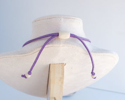 A purple adjustable cord necklace with wooden beads displayed on a cream-colored fabric jewelry bust.