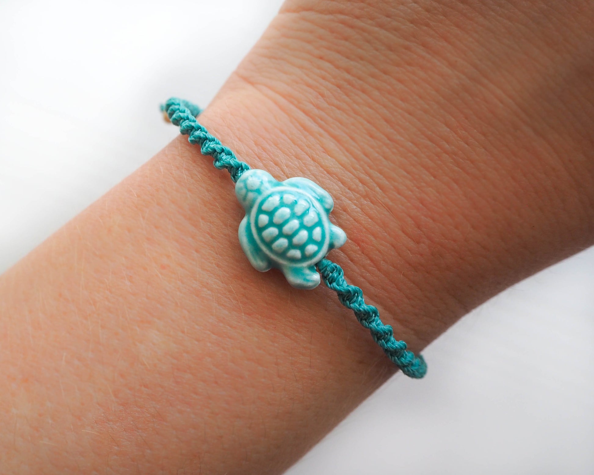 A photo displaying the entire Turquoise Green Ceramic Turtle Braided Bracelet, elegantly worn on a wrist. The bracelet adds a touch of nature-inspired sophistication to the outfit, handmade coastal jewelry, tartaruga, ocean inspired 