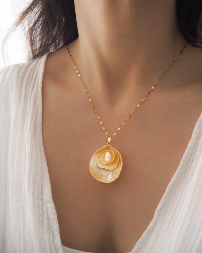 Model wearing a gold chain necklace with a pendant made from layered yellow jingle shells with a layer of mother-of-pearl and a small white freshwater pearl in the center. The jingle shells or saddle oyster shells are handpicked from the beaches of Portugal. Set on a gold stainless steel chain. 