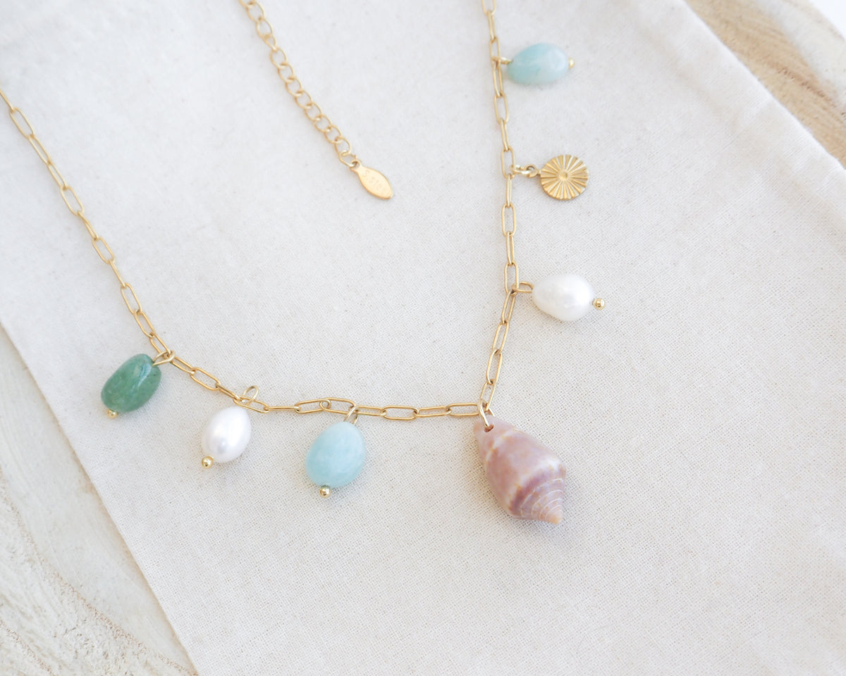 A gold charm necklace with a cone shell, ivory freshwater pearls and green aventurine gemstone beads on cotton displayed. Made with stainless steel chain. The shell is a Mediterranean Cone Shell handpicked from the beaches of Portugal. 