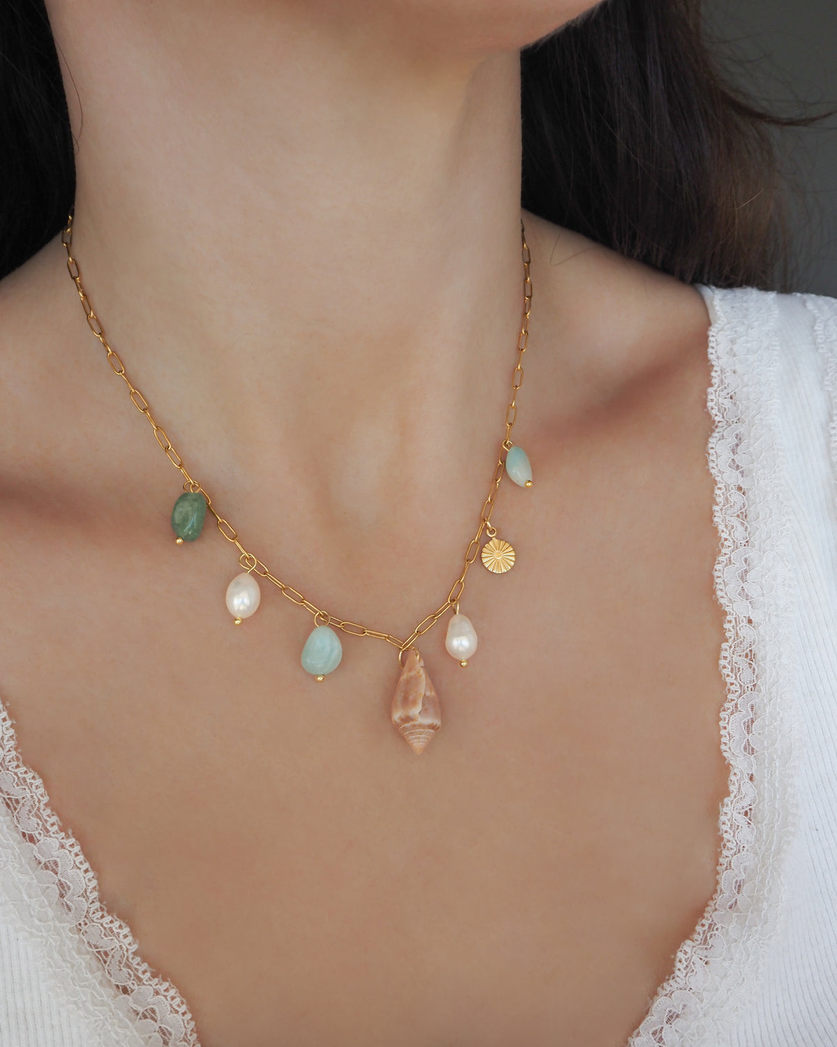 Model wearing a gold charm necklace with a cone shell, ivory freshwater pearls and green aventurine gemstone beads. Made with stainless steel chain. The shell is a Mediterranean Cone Shell handpicked from the beaches of Portugal. 