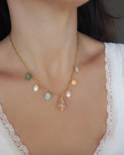 Model wearing a gold charm necklace with a cone shell, ivory freshwater pearls and green aventurine gemstone beads. Made with stainless steel chain. The shell is a Mediterranean Cone Shell handpicked from the beaches of Portugal. 