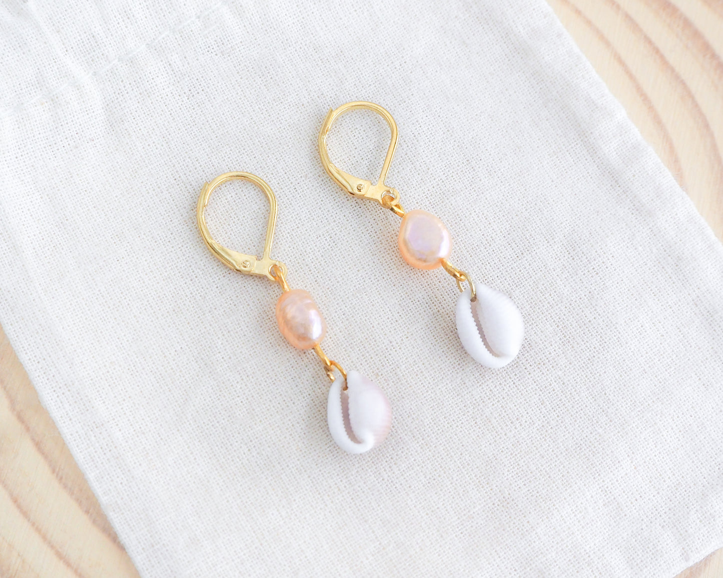 Gold Tiny Cowrie Seashell Pearl Earrings on display. 18k gold stainless steel cowrie pearl earrings handpicked from Portugal