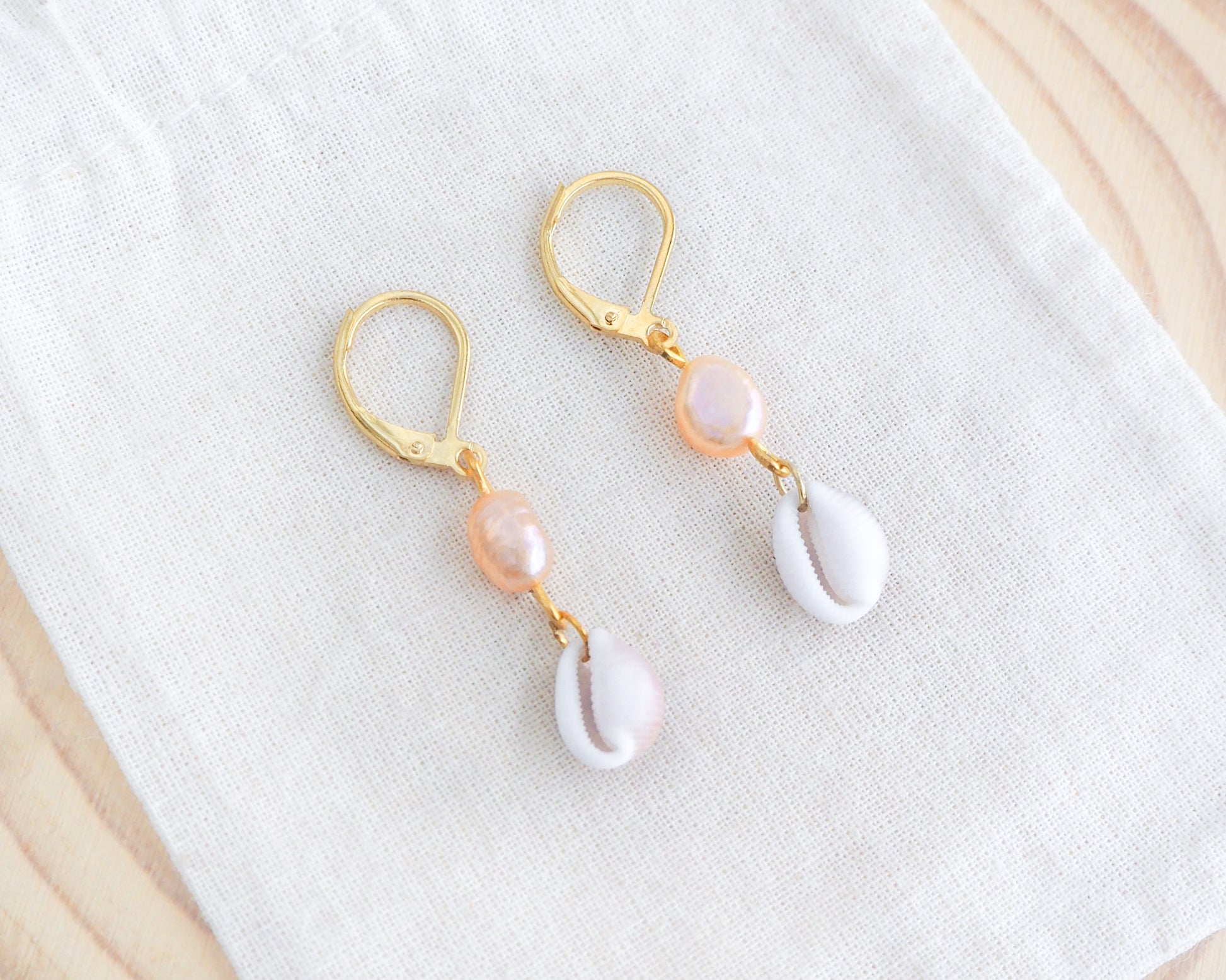 Gold Tiny Cowrie Seashell Pearl Earrings on display. 18k gold stainless steel cowrie pearl earrings handpicked from Portugal
