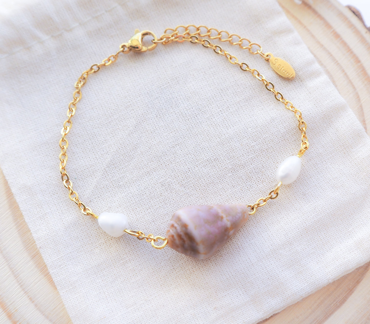 Seaside Sophistication: Close-up of Gold Cone Shell and Freshwater Pearl Bracelet on Gold Chain