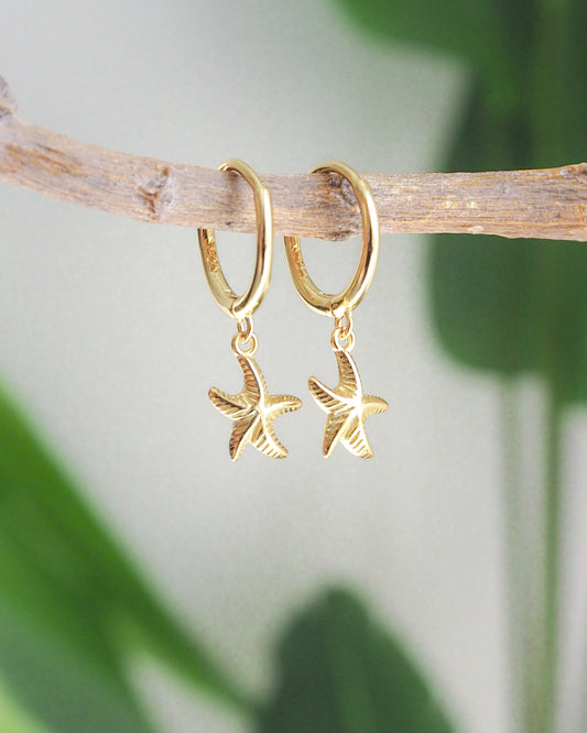 Tiny starfish hoop earrings made of 925 vermeil gold, front view with green plant background