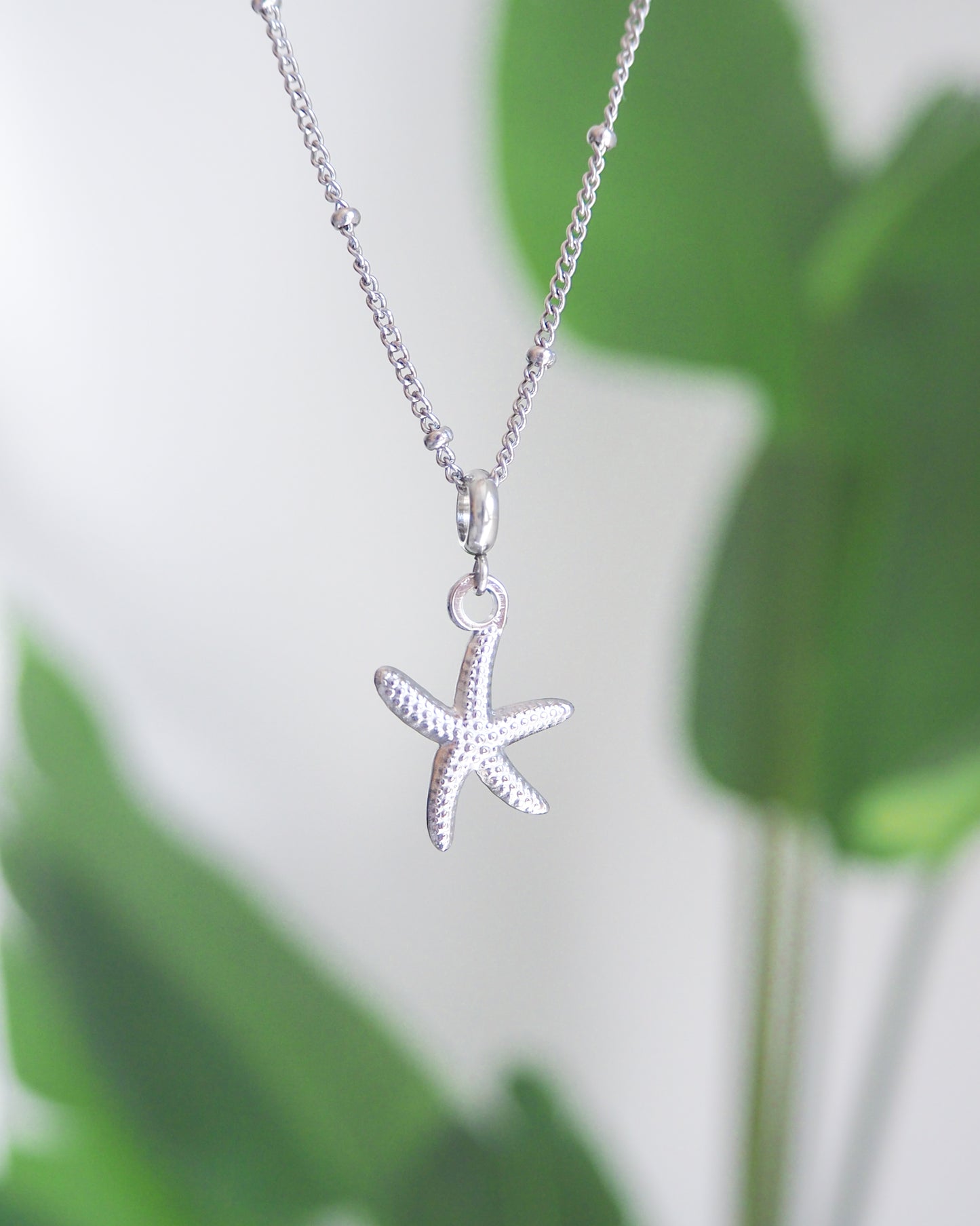 Silver starfish pendant necklace with a green leafy background. Silver Starfish Sea Star Necklace, Seabylou, Hypoallergenic Stainless Steel Bead Chain, Ocean Inspired Jewelry, beach girl jewellery