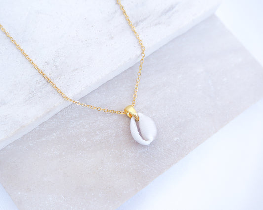 Gold necklace with a tiny white cowrie pendant on a light gray background. Tiny Cowrie Shell Gold Necklace, European Cowrie Shell Necklace, Trivia monacha shell, Portuguese cowrie shell jewelry