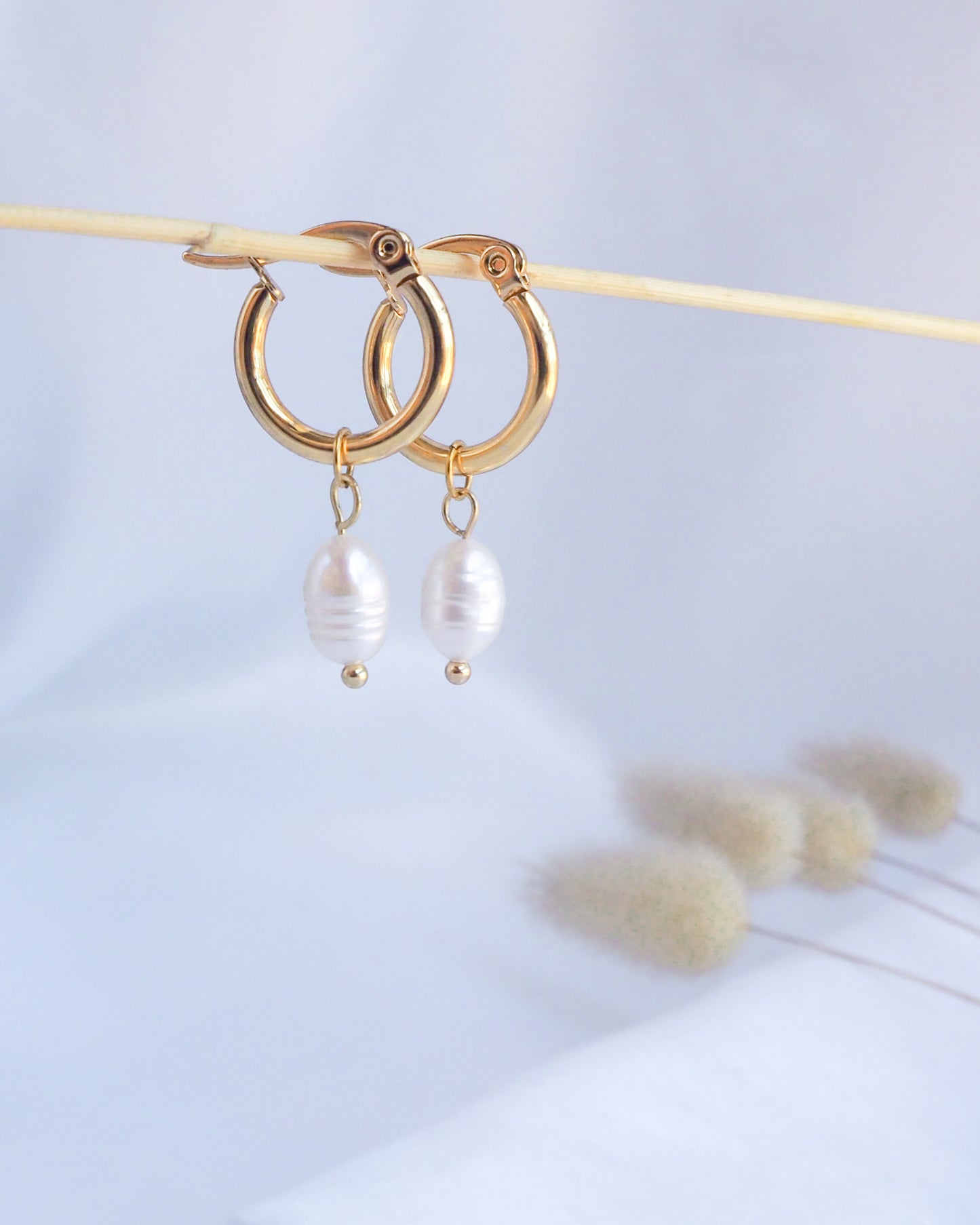 Gold hoop earrings with pearl drops on a light background. Gold Ivory White Pearl Earrings close up
