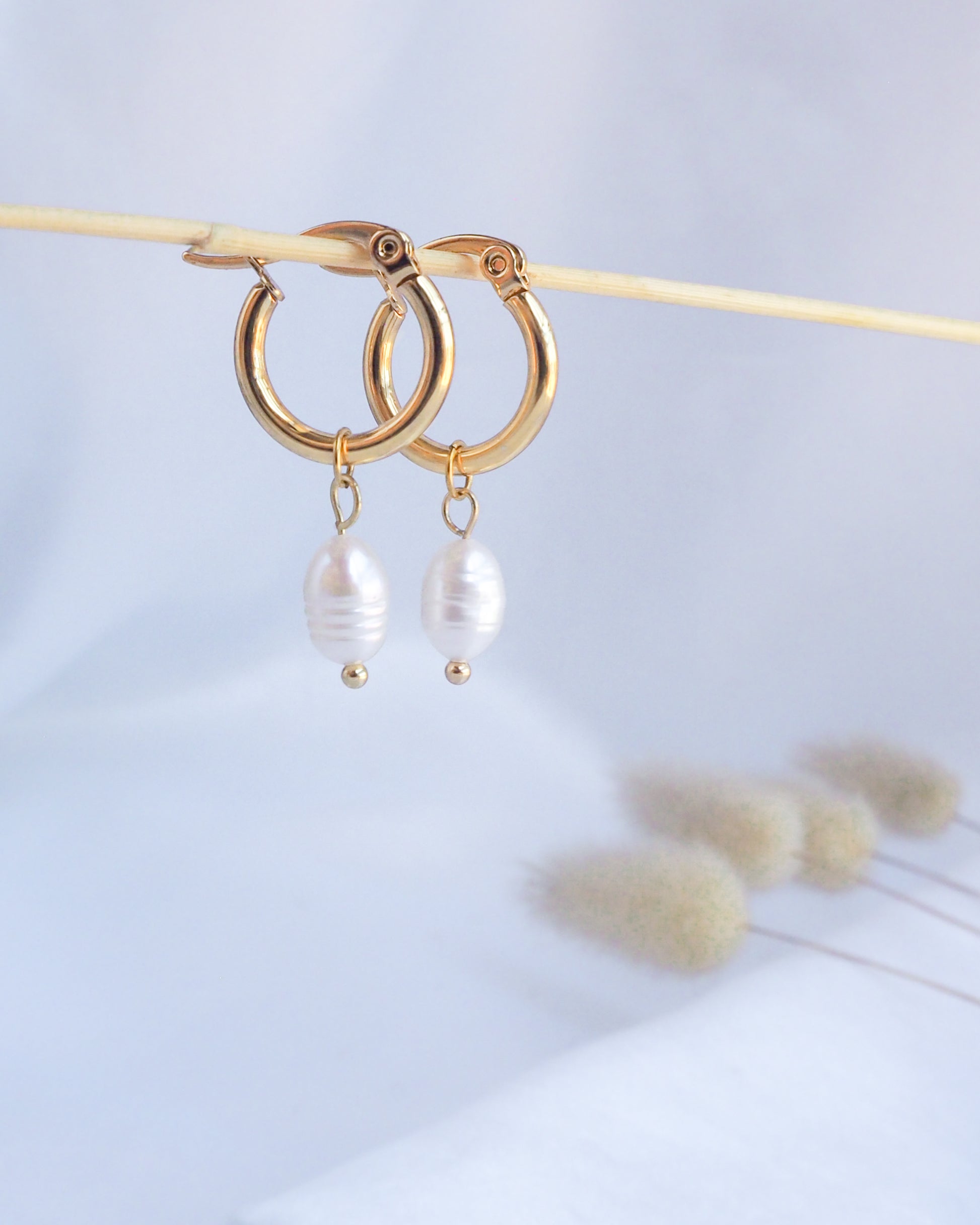 Gold hoop earrings with pearl drops on a light background. Gold Ivory White Pearl Earrings close up