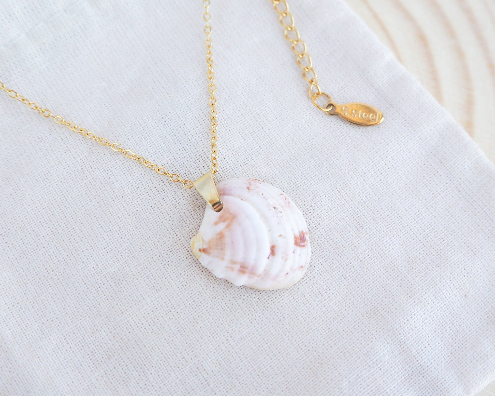 A white peach banded Venus shell necklace on a gold stainless steel chain, displayed on a white fabric background.