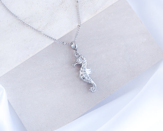 Silver seahorse pendant necklace on a light gray background. Silver Seahorse Necklace on stone. Silver stainless steel chain