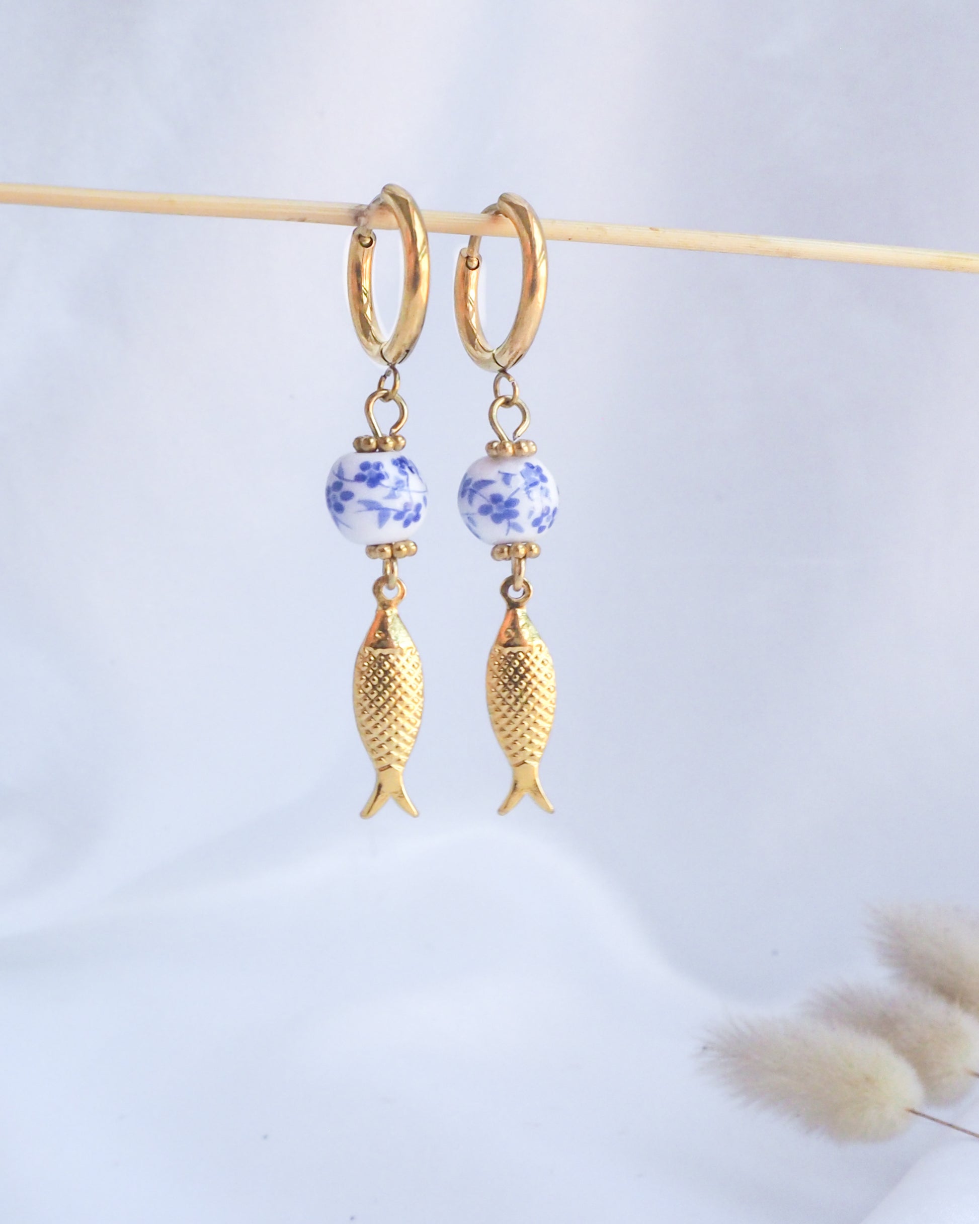 Gold fish-shaped earrings with blue floral beads on a light gray background. Gold Sardine Portuguese Ceramic Earrings