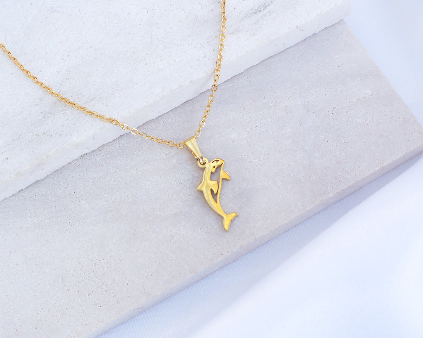 Gold Orca Killer Whale Necklace displayed on stone