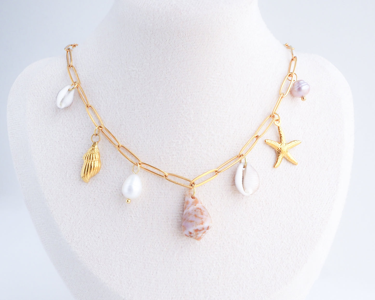 Gold Ocean Shell Charm Necklace on neck, tiny cone and cowrie shells, freshwater pearls, starfish sea star and whale tail pendants. 