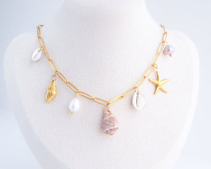 Gold Ocean Shell Charm Necklace on neck, tiny cone and cowrie shells, freshwater pearls, starfish sea star and whale tail pendants. 