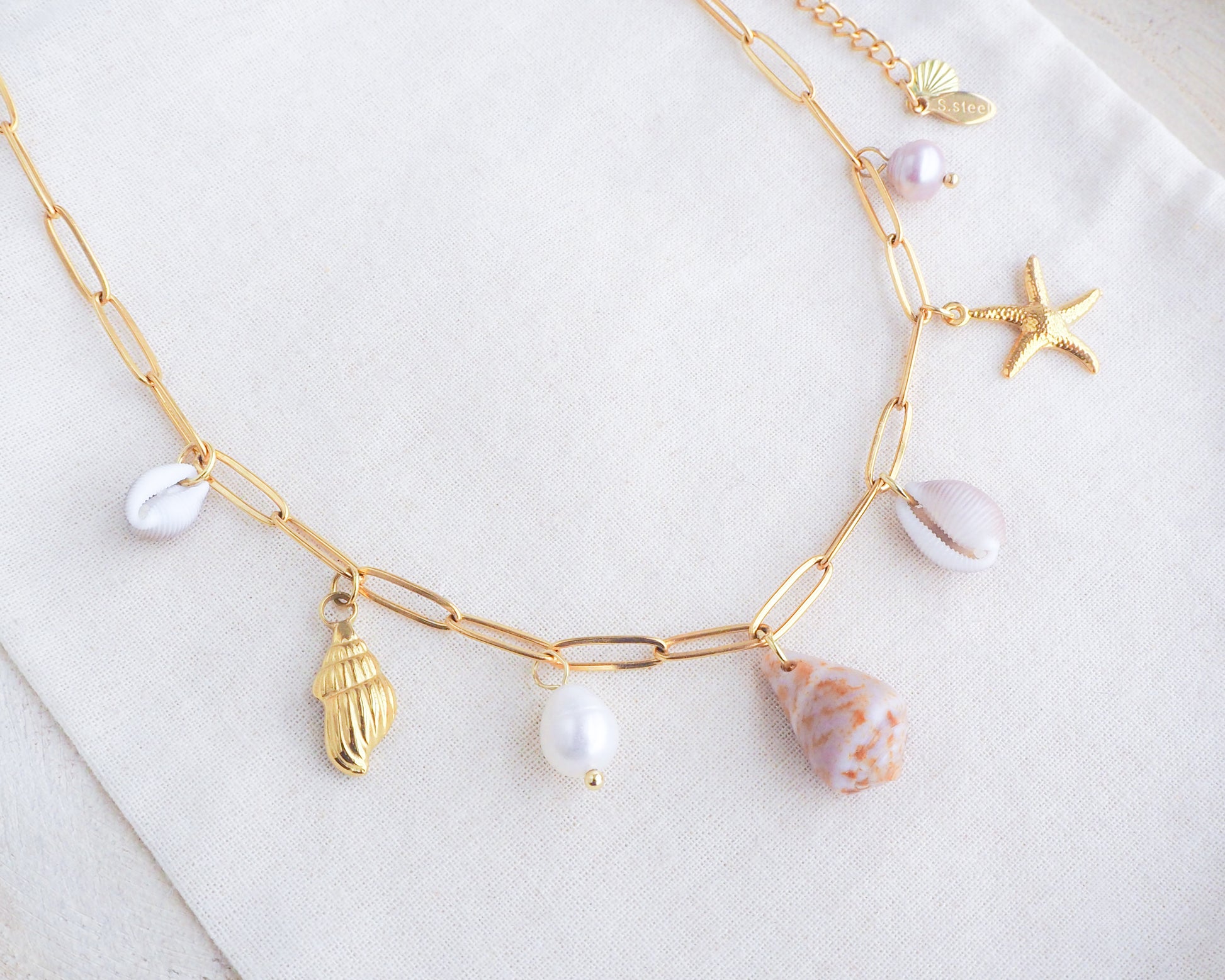 Gold Ocean Shell Charm Necklace on display tiny cone and cowrie shells, freshwater pearls, starfish sea star and whale tail pendants. Made with a 18k gold stainless steel chain. The shells are handpicked from Portugal. 