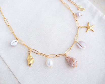 Gold Ocean Shell Charm Necklace on display tiny cone and cowrie shells, freshwater pearls, starfish sea star and whale tail pendants. Made with a 18k gold stainless steel chain. The shells are handpicked from Portugal. 