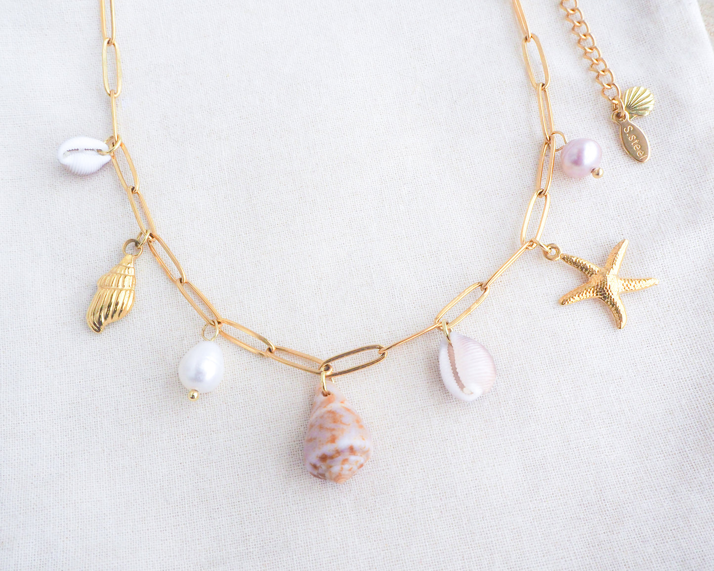 Front view of Gold Ocean Shell Charm Necklace on display tiny cone and cowrie shells, freshwater pearls, starfish sea star and whale tail pendants. Made with a 18k gold stainless steel chain. The shells are handpicked from Portugal. 