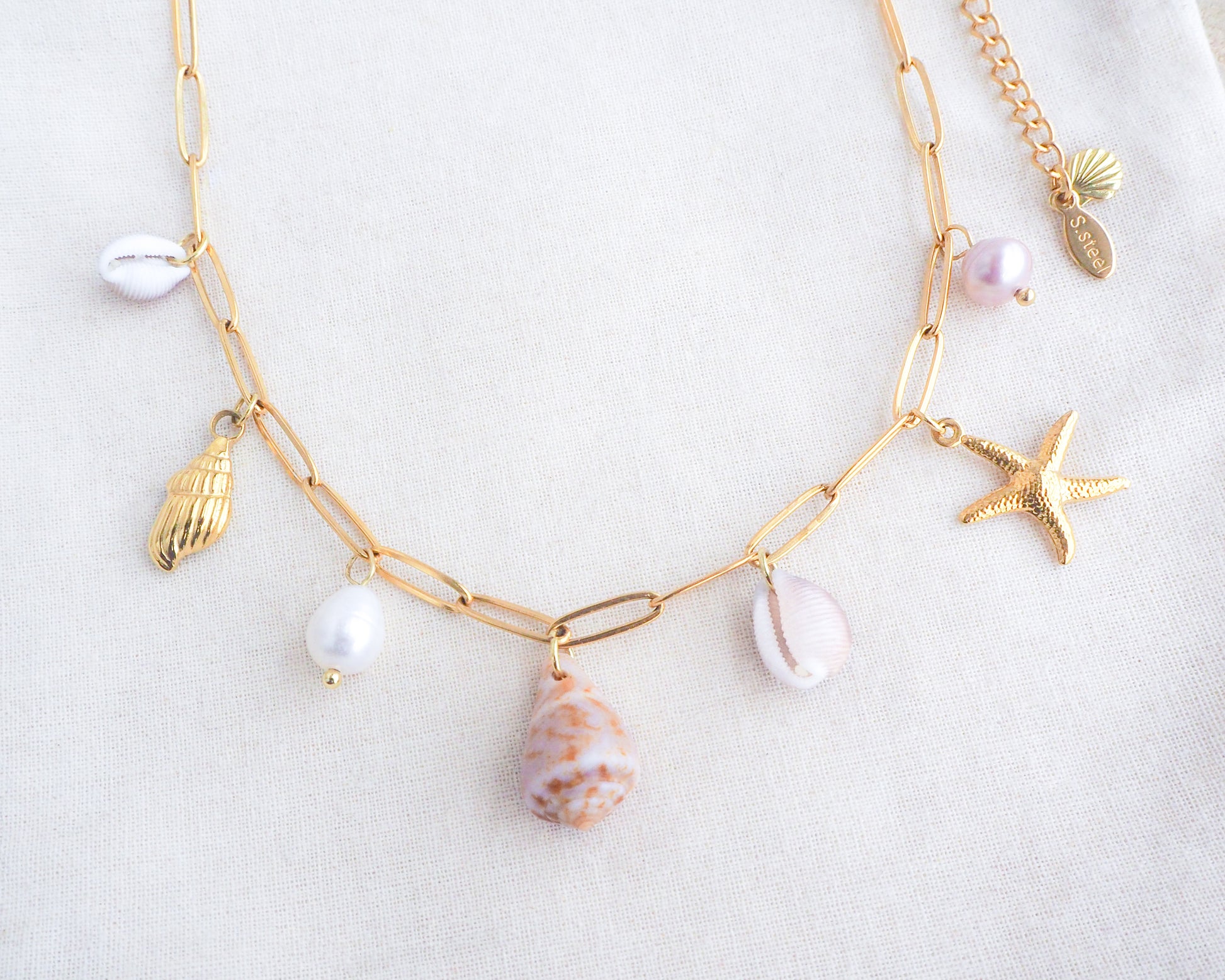 Front view of Gold Ocean Shell Charm Necklace on display tiny cone and cowrie shells, freshwater pearls, starfish sea star and whale tail pendants. Made with a 18k gold stainless steel chain. The shells are handpicked from Portugal. 