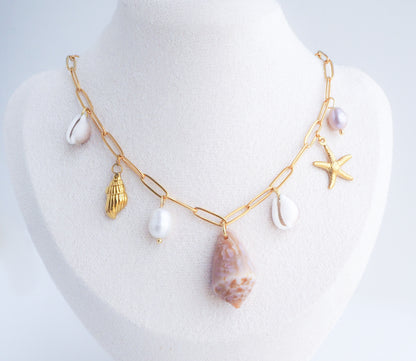 Gold necklace with various charms on a mannequin bust against a white background. Gold Ocean Shell Charm Necklace on mannequin, with cone and cowrie shells, freshwater pearls, starfish sea star shell pendants. 