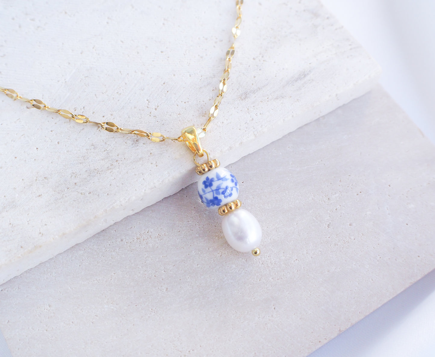 Azulejo Ceramic Tile Pearl Gold Necklace from Portugal. Close up of Gold Azulejo Pearl Necklace from Portugal, Lisbon Tile Jewelry. Made with premium 18k gold stainless steel chain, a ceramic bead and white freshwater pearl. The ceramic bead is showing a flower pattern with white and blue.