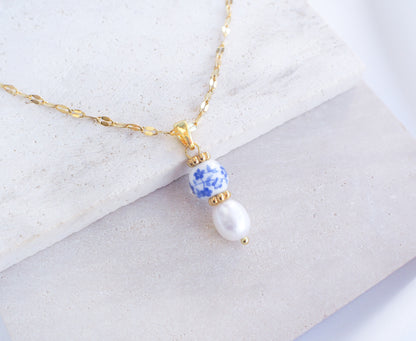 Azulejo Ceramic Tile Pearl Gold Necklace from Portugal. Close up of Gold Azulejo Pearl Necklace from Portugal, Lisbon Tile Jewelry. Made with premium 18k gold stainless steel chain, a ceramic bead and white freshwater pearl. The ceramic bead is showing a flower pattern with white and blue.