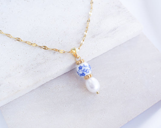 Azulejo Ceramic Tile Pearl Gold Necklace from Portugal. Close up of Gold Azulejo Pearl Necklace from Portugal, Lisbon Tile Jewelry. Made with premium 18k gold stainless steel chain, a ceramic bead and white freshwater pearl. The ceramic bead is showing a flower pattern with white and blue.